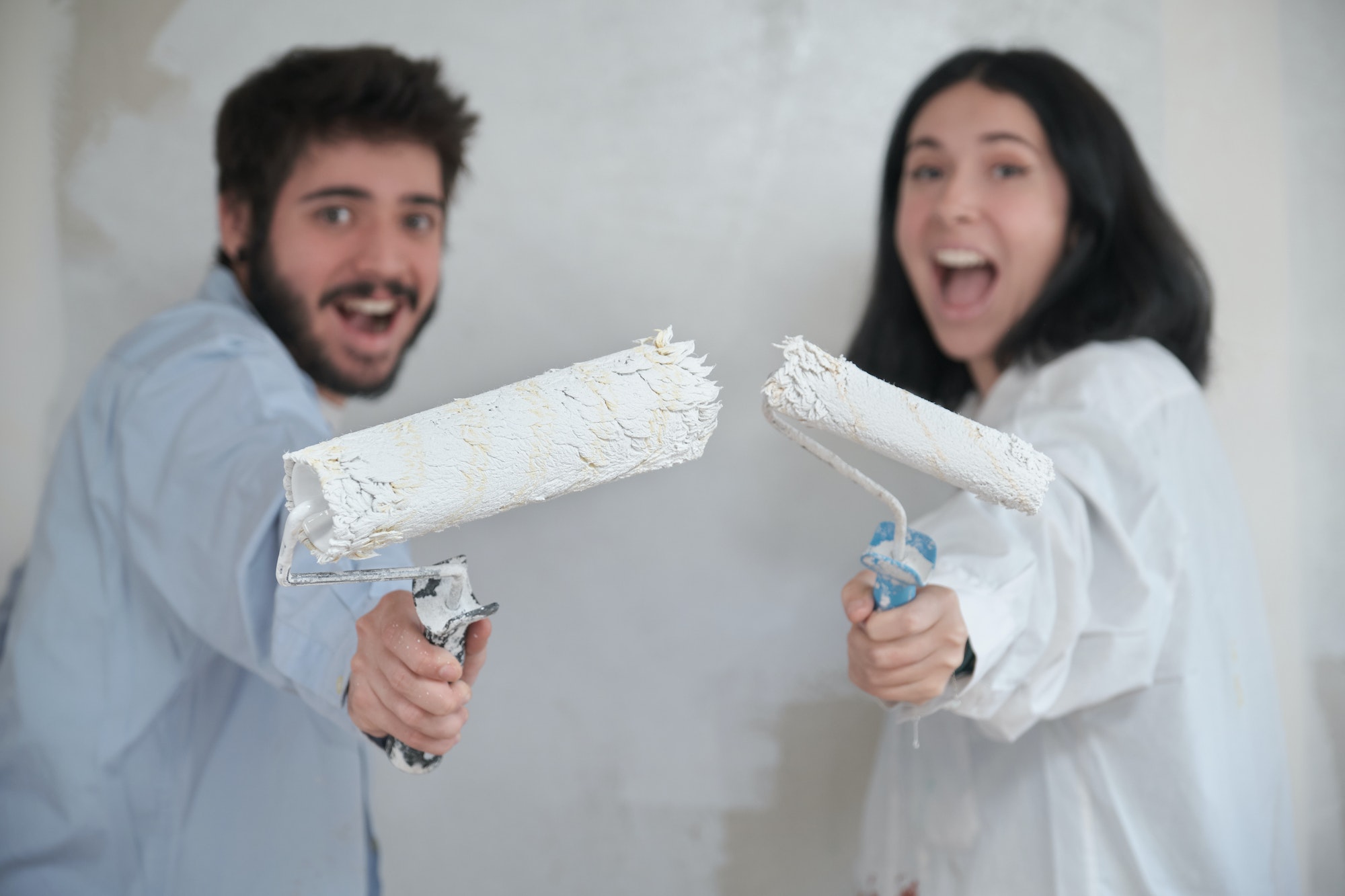 Young couple holding paint rollers and smiling painting their new house.